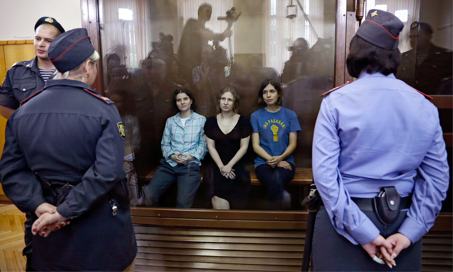 Feminist punk group Pussy Riot members, from left, Yekaterina Samutsevich, Maria Alekhina and Nadezhda Tolokonnikova sit in a glass cage at a court room in Moscow, Russia on Friday, Aug 17, 2012. The women, two of whom have young children, are charged with hooliganism connected to religious hatred but the case is widely seen as a warning that authorities will only tolerate opposition under tightly controlled conditions. T-shirt on right worn by Tolokonnikova is Spanish and translates to "They shall not pass", a slogan often used to express determination to defend a position against an enemy. (AP Photo/Sergey Ponomarev)